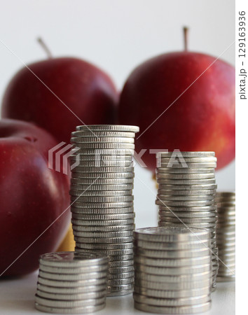 Concept photo of fruits cost. Three red apples and columns of coins closeup stock photo 129163936