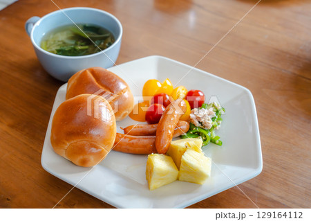 ロールパンとウインナー、サラダや果物が並ぶ洋風朝食セット 129164112