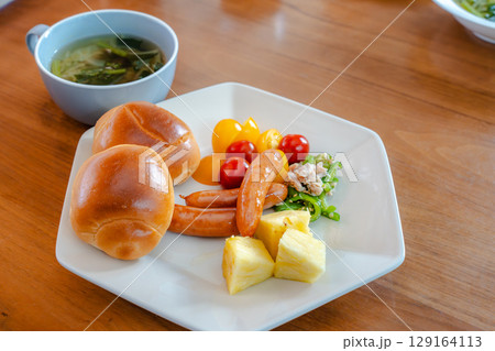 ロールパンとウインナー、サラダや果物が並ぶ洋風朝食セット 129164113