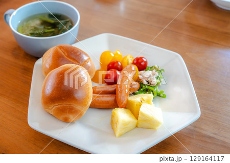 ロールパンとウインナー、サラダや果物が並ぶ洋風朝食セット ロールパンとウインナー、サラダや果物が並ぶ洋風朝食セット 129164117