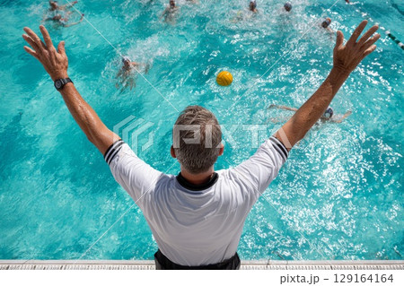 Water polo coach directing players in a vibrant swimming pool during an intense match 129164164