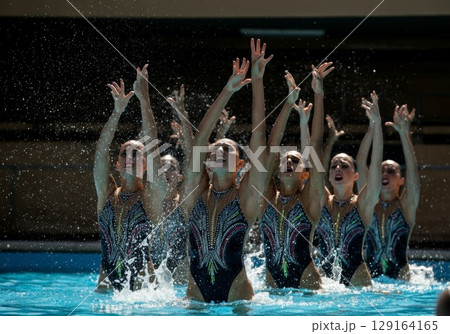 Synchronized swimmers performing a dynamic routine in a bright blue pool with splashes of water 129164165