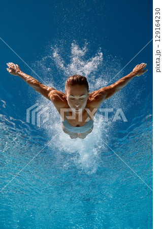 Diver gracefully plunges into clear blue water, showcasing athleticism and precision in motion 129164230