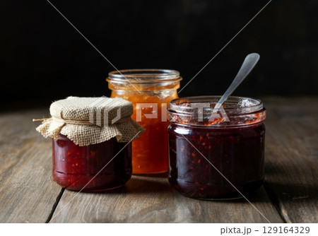 Jars of homemade fruit preserves with rustic lids on wooden table showcasing vibrant colors 129164329