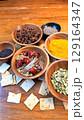 Wooden bowls displaying aromatic spices star anise, cumin, turmeric, dried chilies, cinnamon, coriander seeds, cardamom beside rustic crackers on wooden surface 129164347