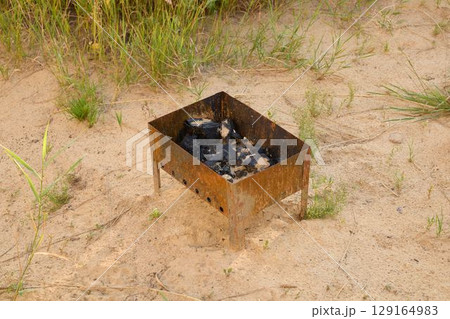 A Rusty Fire Pit Nestled in Soft Sand Surrounded by Charcoal Perfectly Ready for Use When Needed 129164983