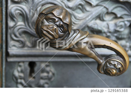 Doorhandle with grimace face and lock at a side portal of the cathedral of Cologne, NRW, Germany 129165388