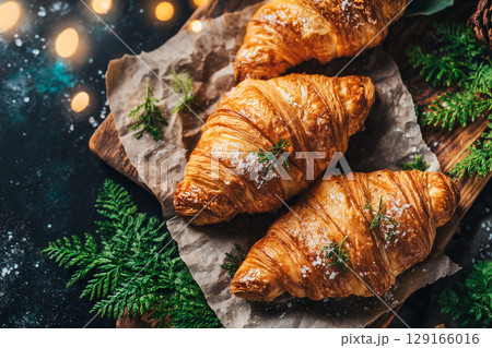 Freshly Baked Croissants on Rustic Paper Surrounded by Greenery and Warm Lights 129166016