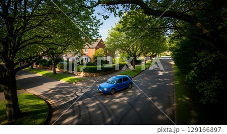 Blue Car Driving On Asphalt Road Through Lush Green Trees in Residential Area During Daylight 129166897