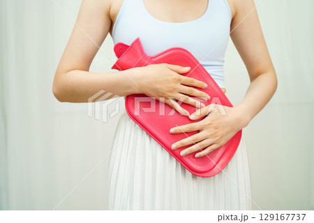 Woman using hot water bottle to relieve menstrual abdominal pain. Woman using hot water bottle to relieve menstrual abdominal pain. 129167737