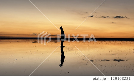 ウユニ塩湖の鏡面に映る、空を見上げる横向きの男性シルエット（夕暮れ・ボリビア） 129168221