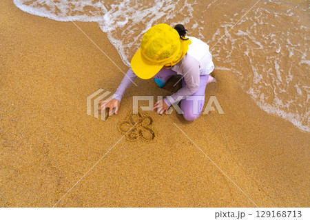 Asian girl playing in the sand by the sea, draw flower and smile in the sand 129168713