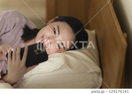 布団の中でスマートフォンを操作する若い女性　ライフスタイルイメージ 129170143