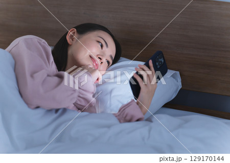 布団の中でスマートフォンを操作する若い女性 ライフスタイルイメージ 布団の中でスマートフォンを操作する若い女性 ライフスタイルイメージ 129170144