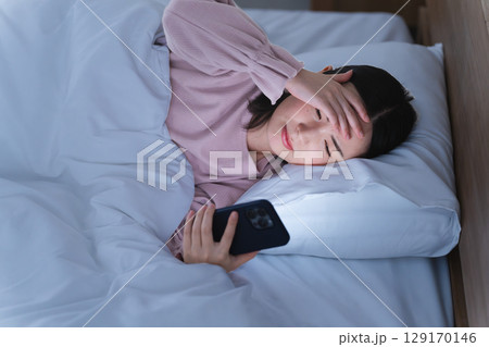 布団の中でスマートフォンを操作する若い女性　ライフスタイルイメージ 129170146