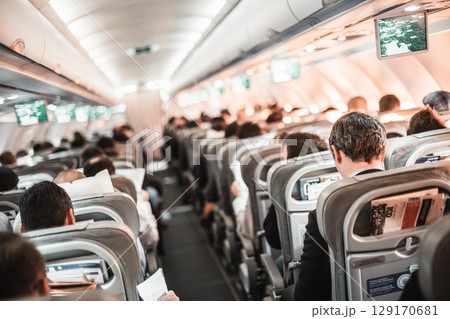 Interior of airplane with passengers on seats and stewardess in uniform walking the aisle, serving people. Commercial economy flight service concept 129170681