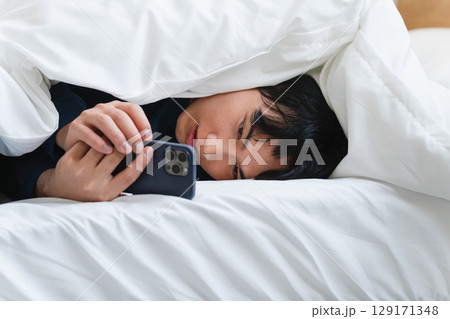 布団にくるまりスマートフォンを操作している若い男性 ライフスタイルイメージ 布団にくるまりスマートフォンを操作している若い男性 ライフスタイルイメージ 129171348