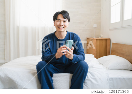 ベッドの上でスマートフォンを操作する若い男性　ライフスタイルイメージ 129171566