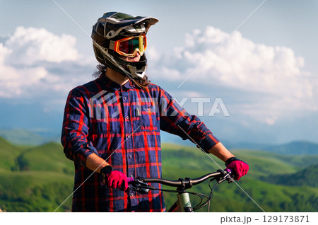 Portrait of a cyclist standing with his bicycle against a dramatic sky with cumulus clouds. Handsome young man biking in the countryside Portrait of a cyclist standing with his bicycle against a dramatic sky with cumulus clouds. Handsome young man biking in the countryside 129173871