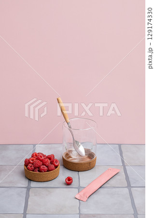 Bowl with fresh red raspberries next to an empty glass and an unopened pink stick pack. Bowl with fresh red raspberries next to an empty glass and an unopened pink stick pack. 129174330