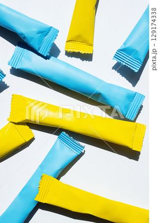 Yellow and blue stick pack sachets scattered on a white background. 129174338