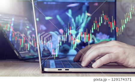 hands typing on laptop with green and red candlestick chart overlay, symbolizing rising market trends and investments. 129174371