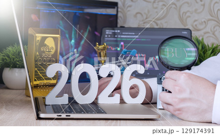Concept of 2026 financial opportunities featuring gold bar, house model, and magnifying glass with BUY text over market chart on laptop. 129174391