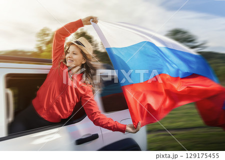 Woman celebrating Russia Day by waving the Russian flag from a car during a road trip, embodying pride and independence outdoors Woman celebrating Russia Day by waving the Russian flag from a car during a road trip, embodying pride and independence outdoors 129175455