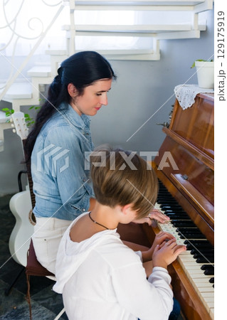 A young girl receives a piano lesson from her teacher. They are both focused on the music. A young girl receives a piano lesson from her teacher. They are both focused on the music. 129175919