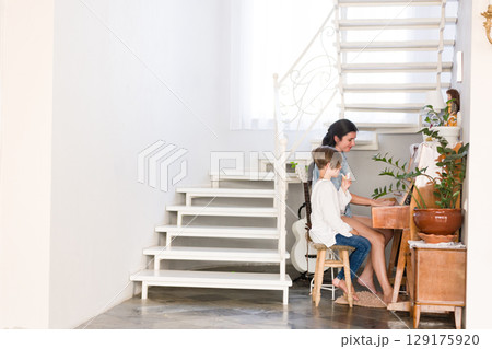 A woman and child enjoy a musical moment together at an old piano in a bright, airy home. 129175920