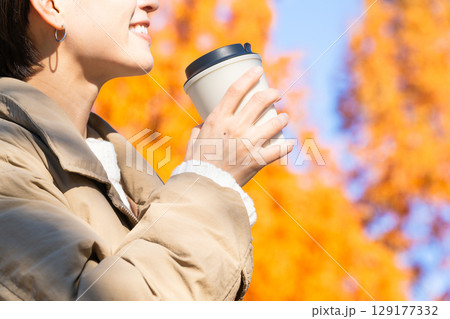 紅葉を楽しみながらホットドリンクを飲む女性　ライフスタイルイメージ 129177332