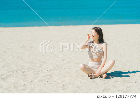 砂浜に座る水着の若い女性 129177774