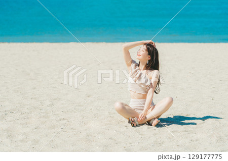 砂浜に座る水着の若い女性 129177775