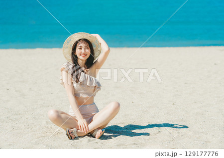 砂浜に座る水着の若い女性 129177776