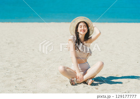 砂浜に座る水着の若い女性 129177777