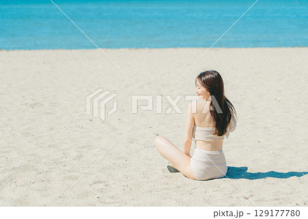 砂浜に座る水着の若い女性 129177780