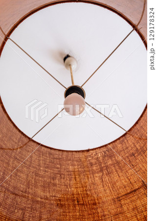 Close-up of a glowing ceiling pendant lamp with a natural straw shade. Warm interior lighting. Close-up of a glowing ceiling pendant lamp with a natural straw shade. Warm interior lighting. 129178324