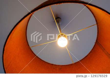 Close-up of a glowing ceiling pendant lamp with a natural straw shade. Warm interior lighting. Close-up of a glowing ceiling pendant lamp with a natural straw shade. Warm interior lighting. 129178329