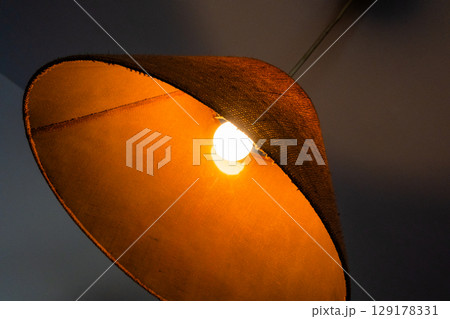 Close-up of a glowing ceiling pendant lamp with a natural straw shade. Warm interior lighting. 129178331