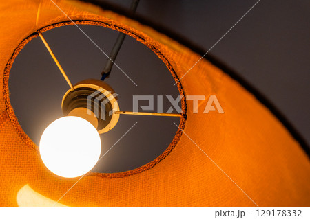 Close-up of a glowing ceiling pendant lamp with a natural straw shade. Warm interior lighting. Close-up of a glowing ceiling pendant lamp with a natural straw shade. Warm interior lighting. 129178332