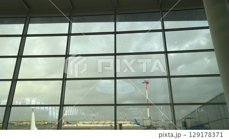 Planes and the exterior of an airport seen through the waiting room window on a very cloudy day. 129178371