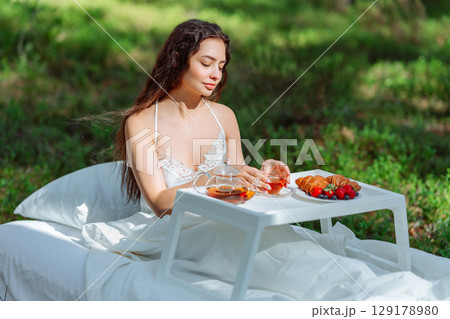 Young woman has breakfast in bed in a summer forest Young woman has breakfast in bed in a summer forest 129178980