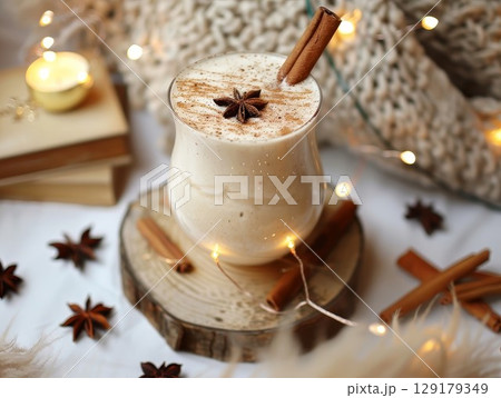 Creamy drink with cinnamon sticks and star anise on wooden base. Cozy setup with fairy lights for holiday themes. Perfect for winter or festive decor. 129179349