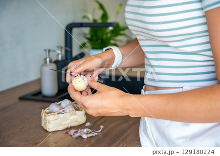 Female hands peeling Chinese single clove garlic on kitchen countertop. Cooking process, natural seasoning, and preparation of fresh ingredient. 129180224