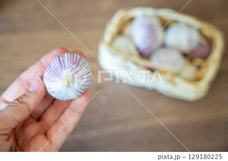 Female hand holding a head of Chinese single clove garlic with a basket full of garlic in the background. Natural food ingredient and kitchen preparation. 129180225
