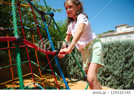 Smiling Girl Enjoys Outdoor Activity on Colorful Rope Playground on a Bright Sunny Day 129182140