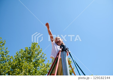 Child Celebrating on a Playground Rope Structure on a Sunny Day Outdoors 129182144