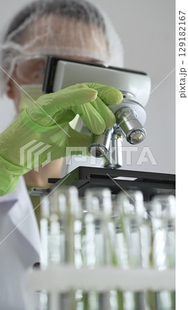 Close up of scientific precision involving green gloved hands adjusting microscope lens, blurred laboratory glassware highlighting medical investigation. Medicine, laboratory and science concept 129182167