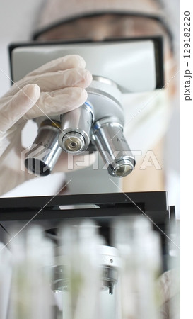 Close up of white gloved hand of a scientist adjusting a microscope in a laboratory. Medicine, health care and science concept Close up of white gloved hand of a scientist adjusting a microscope in a laboratory. Medicine, health care and science concept 129182220