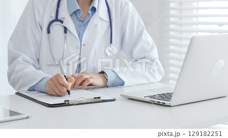 Female doctor documents patient information while working with digital devices at workplace in office. Medicine and healthcare concept 129182251